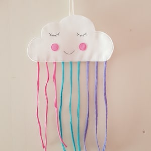 May include: A white felt cloud with a smiling face and pink cheeks, hanging from a hook.  It has rainbow-colored fabric strips hanging from the bottom.