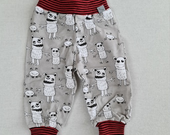 Op de afbeelding: Grijze babybroek met een zwart-witte monsterprint en rood-zwarte gestreepte tailleband en boorden. De broek heeft een klein wit label met het woord "Pridd" op de tailleband.