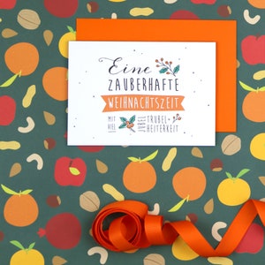 May include: A white card with the text "Eine zauberhafte Weihnachtszeit mit viel Jubel, Trubel & Heiterkeit" on a green background with orange and red illustrations of fruit and nuts. The card is tied with an orange ribbon.