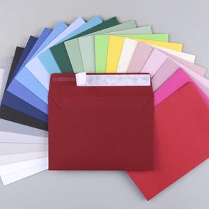 Op de afbeelding: Een waaier van kleurrijke enveloppen in verschillende tinten blauw, groen, geel, roze en rood. De enveloppen zijn in een halve cirkel gerangschikt met de rode envelop in het midden.