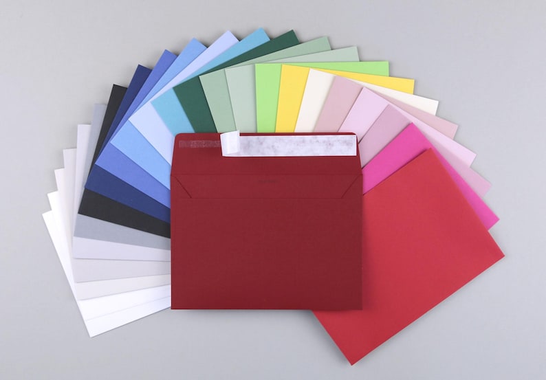 Op de afbeelding: Een waaier van kleurrijke enveloppen in verschillende tinten blauw, groen, geel, roze en rood. De enveloppen zijn in een halve cirkel gerangschikt met de rode envelop in het midden.