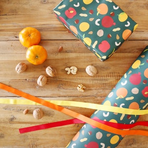 May include: A flat lay of a wooden surface with two orange mandarins, a variety of nuts, and two pieces of green and white patterned wrapping paper. The wrapping paper has a design of fruit and nuts.