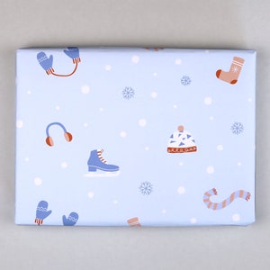 May include: Blue wrapping paper with a winter theme. The paper features a repeating pattern of mittens, earmuffs, ice skates, hats, and snowflakes on a light blue background.