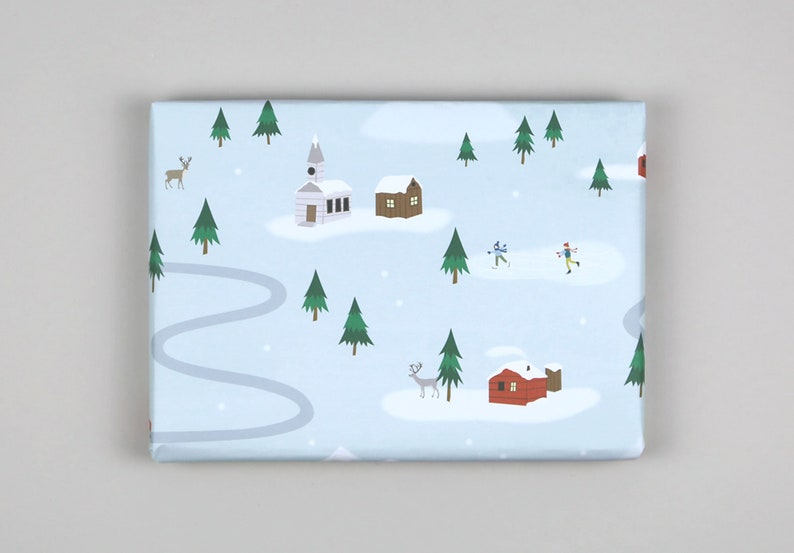 Puede incluir: Un papel de regalo azul y blanco con una escena de pueblo de invierno. El papel presenta casas, &aacute;rboles, una iglesia y personas patinando sobre hielo. Tambi&eacute;n hay ciervos y un camino sinuoso.