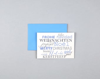 Puede incluir: Una tarjeta blanca con las palabras "Frohe Weihnachten", "feliz navidad", "joyeux Noel", "Merry Christmas", "buon Natale", "god jul" y "vrolijk kerstfeest" en diferentes idiomas. La tarjeta está sobre un fondo azul claro.