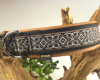 May include: A brown leather dog collar with a black and white patterned trim. The collar has a silver buckle and a D-ring. The brand name "skreytt" is visible on the collar.