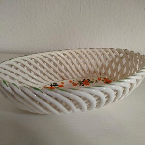 Könnte beinhalten: Weißer, geflochtener Korb aus Keramik mit grünem Rand und einem floralen Design in Orange, Grün und Schwarz.