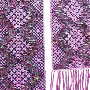 May include: A pink crocheted scarf with a geometric pattern and fringe. The scarf has a woven design with colorful threads.
