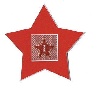 Puede incluir: Un marco rojo en forma de estrella con un borde plateado. Dentro del marco hay una estrella roja con un centro blanco, sobre un fondo estampado blanco y rojo.