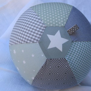 Könnte beinhalten: Ein mehrfarbiger Patchwork-Ball mit einem Stern in der Mitte. Der Ball besteht aus verschiedenen Stoffen mit verschiedenen Mustern, darunter Gingham, Sterne und geometrische Muster. Der Ball ist hellblau, grün und grau.