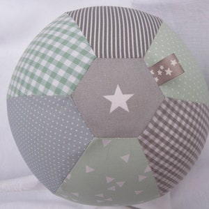 Könnte beinhalten: Ein grüner, grauer und brauner Patchwork-Fußball aus Stoff mit einem weißen Stern auf einem Panel und einem braunen Stoffanhänger mit weißen Sternen auf einem anderen Panel.