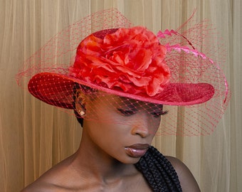 Large red sinamay wedding hat with veil, feathers and flower on top of the hat