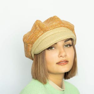 May include: A tan newsboy hat with a textured crown and a solid brim. The hat is made of a woven material and has a classic, stylish design. A fashionable accessory.