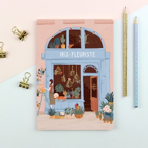 Könnte beinhalten: Eine pastellrosa und blaue Illustration einer Blumengeschäftsfront mit dem Text "IRIS - FLEURISTE" über der Tür. Das Schaufenster ist mit Pflanzen und Blumen gefüllt, und eine Person gießt die Pflanzen. Eine Katze sitzt auf dem Fenstersims.
