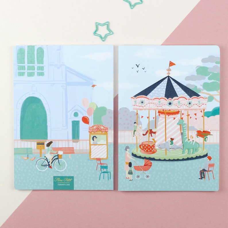 May include: Two illustrated notebooks with a blue background. The left notebook features a building with a green roof and a woman riding a bicycle. The right notebook features a carousel with a teacup, a giraffe, and a dolphin. Both notebooks have the text "Flora Petit Illustrations" on the bottom.