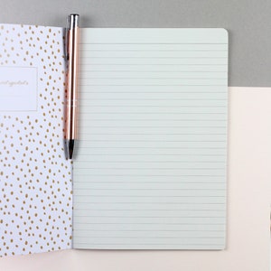 May include: A white notebook with lined pages and a gold pen. The notebook cover has a pattern of gold dots on a white background.