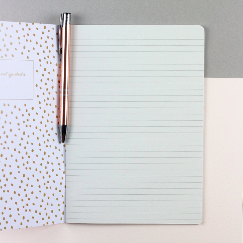 May include: A white notebook with lined pages and a gold pen. The notebook cover has a pattern of gold dots on a white background.