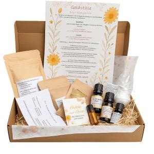 Könnte beinhalten: Ein brauner Karton gefüllt mit verschiedenen Artikeln, darunter kleine Flaschen, Päckchen und ein großes Blatt Papier mit Text und floralen Illustrationen. Die Box enthält ätherische Öle und Badeprodukte.