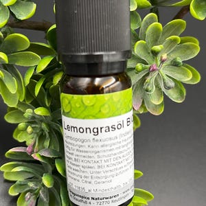 Könnte beinhalten: Eine kleine Braunglasflasche mit schwarzem Schraubverschluss und einem weißen Etikett mit grüner Blattgrafik. Der Text auf dem Etikett lautet Lemongrasöl Bio, Cymbopogon flexuosus, inklusive Sicherheitshinweisen und Firmenangaben.