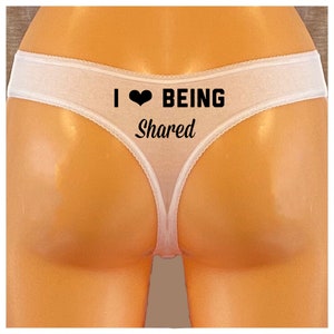 May include: White thong underwear with the text "I ♥ BEING Shared" in black. The underwear has a delicate, lacy trim along the edges.