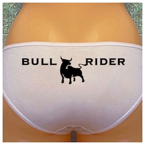 Peut inclure: Sous-vêtements en coton blanc avec une silhouette de taureau noire et le texte "BULL RIDER" imprimé au dos.