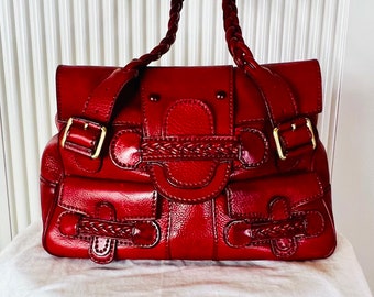May include: A red leather handbag with a braided strap and multiple pockets. The bag has gold hardware and a textured leather finish.