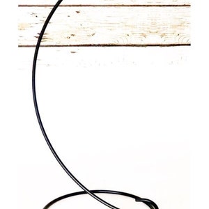 May include: Black metal stand with a circular base and a curved arm with a hook at the top. The stand is designed to hold a hanging ornament or other decorative item.