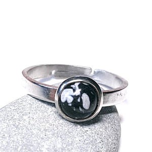 Puede incluir: Anillo ajustable de plata con una piedra redonda en blanco y negro. El anillo está sobre una piedra gris sobre un fondo blanco. La piedra tiene un diseño abstracto.