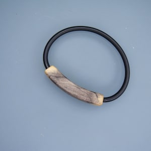 Könnte beinhalten: Ein schwarzes Gummiband mit einem Holzperlen-Akzent. Die Perle ist hellbraun mit dunkelbraunen Streifen.