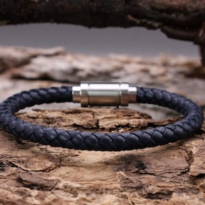 Könnte beinhalten: Ein dunkelblaues geflochtenes Lederarmband mit einem silbernen Magnetverschluss.