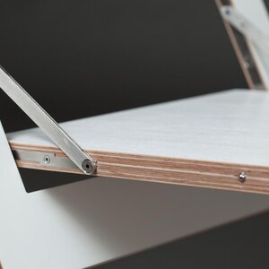 May include: White folding chair with a metal hinge and a white plywood seat. The chair is made of wood and metal.