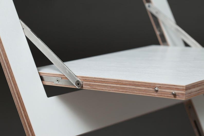 May include: White folding chair with a metal hinge and a white plywood seat. The chair is made of wood and metal.