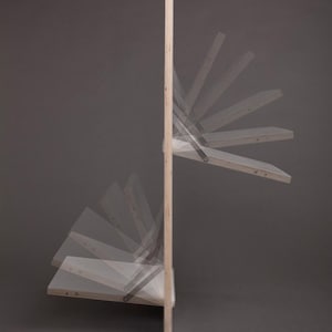 May include: A wooden wall-mounted shelf unit with multiple shelves that fold down. The shelves are made of light wood and have a natural finish. The unit is mounted to a wall and has a simple, modern design.