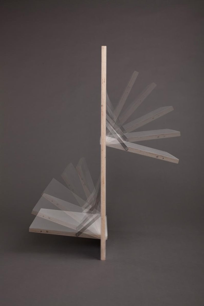 May include: A wooden wall-mounted shelf unit with multiple shelves that fold down. The shelves are made of light wood and have a natural finish. The unit is mounted to a wall and has a simple, modern design.