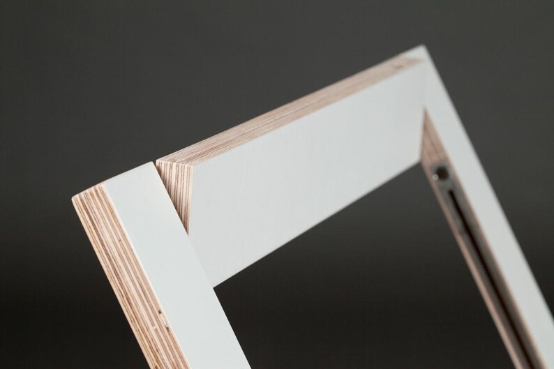 May include: Close-up of a white painted wooden frame with visible layers of plywood. The frame is angled and appears to be part of a larger piece of furniture.