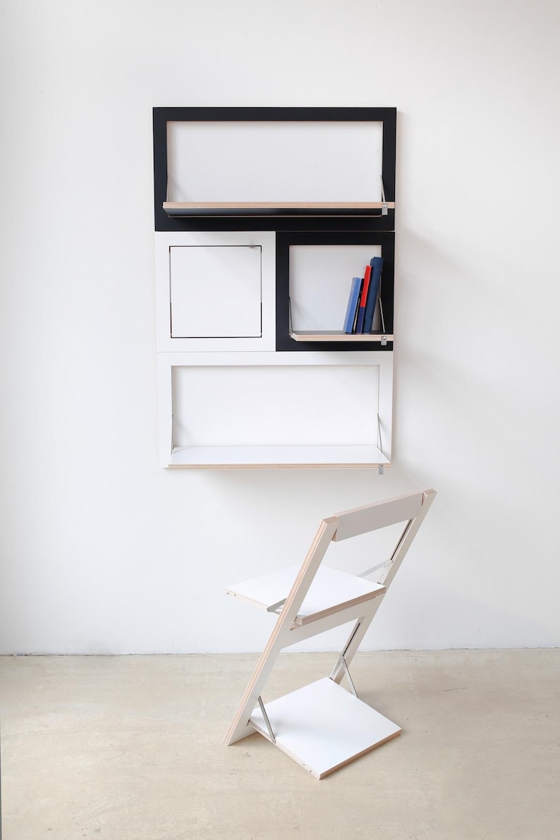 May include: A white and black wall-mounted desk with shelves and a fold-down desk surface. A white folding chair is in front of the desk.