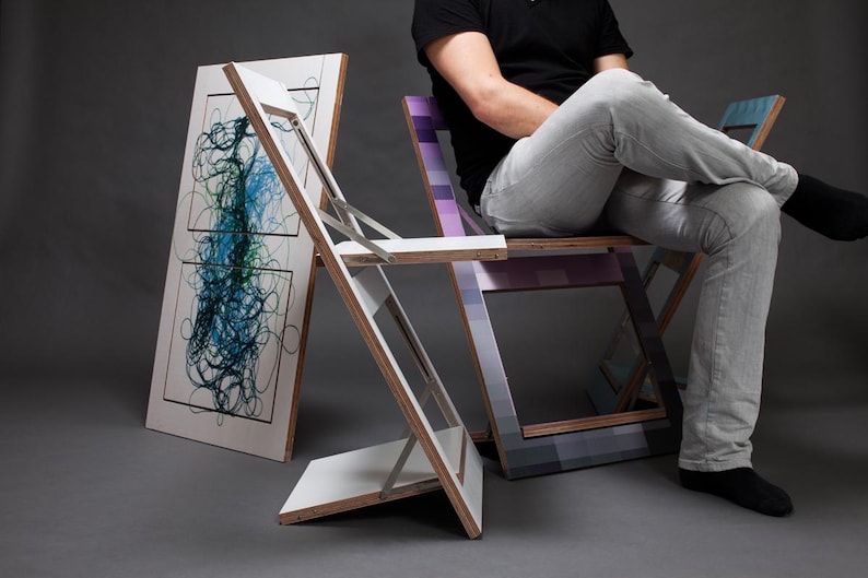 May include: Two folding chairs with colorful geometric patterns and a white folding chair with a blue and green abstract design. The chairs are made of wood and have a metal frame.