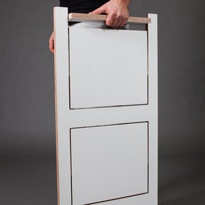May include: A white folding chair with a wooden handle. The chair is made of plywood and has a simple, modern design.