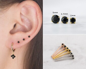 May include: An assortment of black stud earrings and a gold hoop earring with a black flower charm. The stud earrings are shown in various sizes: 2mm, 2.5mm, and 3mm. Several pairs of stud earrings are displayed in gold, silver, and rose gold.