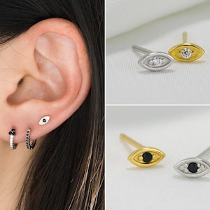 Peut inclure: Boucles d'oreilles en or et argent avec un motif d'œil. Une paire est ornée d'une pierre transparente, l'autre d'une pierre noire. Sont également présentées de petites créoles avec des pierres noires.
