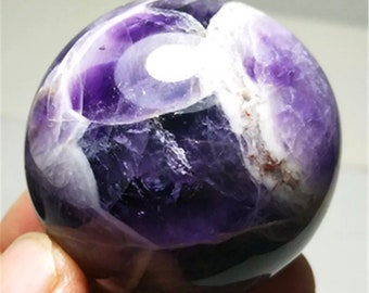 Peut inclure: Une grande sphère d'améthyste polie avec des motifs tourbillonnants de violet et de blanc. La sphère est lisse et a une finition brillante.