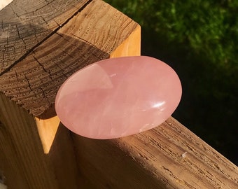 May include: A smooth, pale pink rose quartz heart-shaped stone. The stone is polished and has a glossy finish.