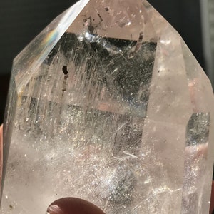 May include: A clear quartz crystal point with a double termination. The crystal has a natural, raw look with visible inclusions and striations. The crystal is clear and translucent, with a slight shimmer.