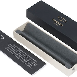 May include: A black and white box with the Parker logo and the text "EST. 1888". The box is open and the inside is lined with gray felt. The box is for a pen.