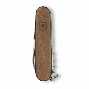 Puede incluir: Una multiherramienta marr&oacute;n y plateada con mango de madera. El mango presenta un escudo con un emblema de cruz. La herramienta incluye un sacacorchos y un llavero. La multiherramienta est&aacute; dise&ntilde;ada para diversos usos.
