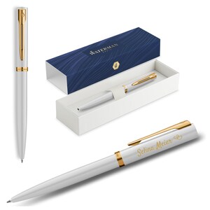 Könnte beinhalten: Ein weißer Waterman-Stift mit goldenen Akzenten, präsentiert in einer weißen Schachtel mit einem marineblauen Deckel. Der Stift trägt den eingravierten Namen "Selina Meier". Der Stift wird aus verschiedenen Blickwinkeln gezeigt.