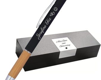 Op de afbeelding: Zwarte pen met een bamboe huls en zilveren accenten. De pen is gegraveerd met de naam "Josefine Trix" en een smiley en twee harten. De pen zit in een zwarte doos met een wit label waarop "Alles Gute zum Geburtstag" staat met een klavertje vier.
