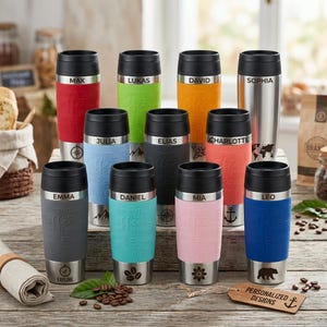 Könnte beinhalten: Eine Sammlung von elf Reisebechern aus Edelstahl mit schwarzen Deckeln und farbigen Silikonmanschetten. Jeder Becher ist mit einem individuellen Namen wie Max, Lukas, David, Sophia, Julia, Elias, Charlotte, Emma, Daniel, Mia und Leo versehen.