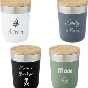 Könnte beinhalten: Vier Edelstahl-Reisebecher mit Bambusdeckeln. Die Becher sind in verschiedenen Farben: weiß, blau, schwarz und grün. Jeder Becher hat ein anderes Design und einen anderen Text. Der weiße Becher hat einen Schmetterling und den Text "Antonia". Der blaue Becher hat Berge und den Text "Emily". Der schwarze Becher hat einen Totenkopf und Knochen und den Text "Michi's Becher". Der grüne Becher hat einen Hund und den Text "Max".