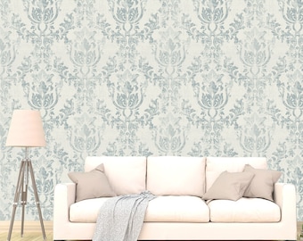 May include: A white couch with a light gray throw blanket and two beige pillows in front of a wall with a light blue and white damask pattern.